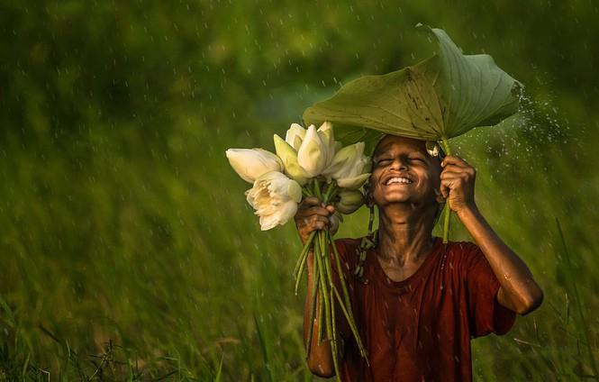 Bức ảnh duy nhất giành chiến thắng của nhiếp ảnh gia @phOWNasaf (Bangladesh) có tên: “Có người tận hưởng cơn mưa, nhưng có người lại khó chịu vì bị ướt” được chụp tại Akkelpur, Joypurhat, Bangladesh. “Đó là một ngày nắng và tôi đã lên kế hoạch đi chụp ảnh. Tôi phát hiện ra cậu bé này đang hái hoa, và chỉ một lát sau mưa bắt đầu trút xuống. Cậu ấy nở nụ cười tươi nhất và thuần khiết nhất trên khuôn mặt khi bị ướt. Đối với tôi, hạnh phúc là một trong những kết quả của đức tin đúng đắn. Niềm tin mang lại cho bạn sự tự tin, và sự tự tin mang đến cho bạn năng lượng. Và khi bạn cảm thấy năng lượng, bạn cười một cách vô thức”, nhiếp ảnh gia viết.