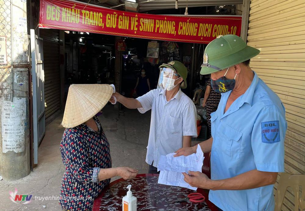 Lực lượng chức năng đo thân nhiệt, kiểm tra thông tin trên phiếu trước khi người dân vào chợ.